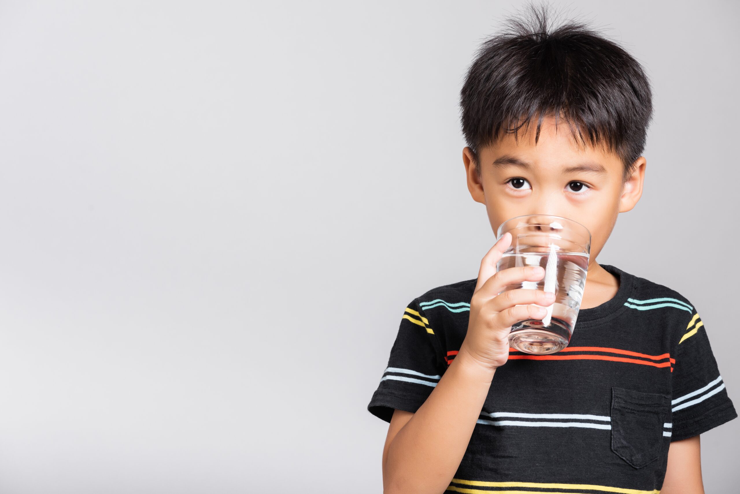 5-6 yaşlarında küçük şirin bir çocuk gülümseyerek stüdyoda camdan tatlı su içiyor, beyaz arka planda izole edilmiş, Asyalı çocuklar okul öncesi, Günlük yaşam sağlığı