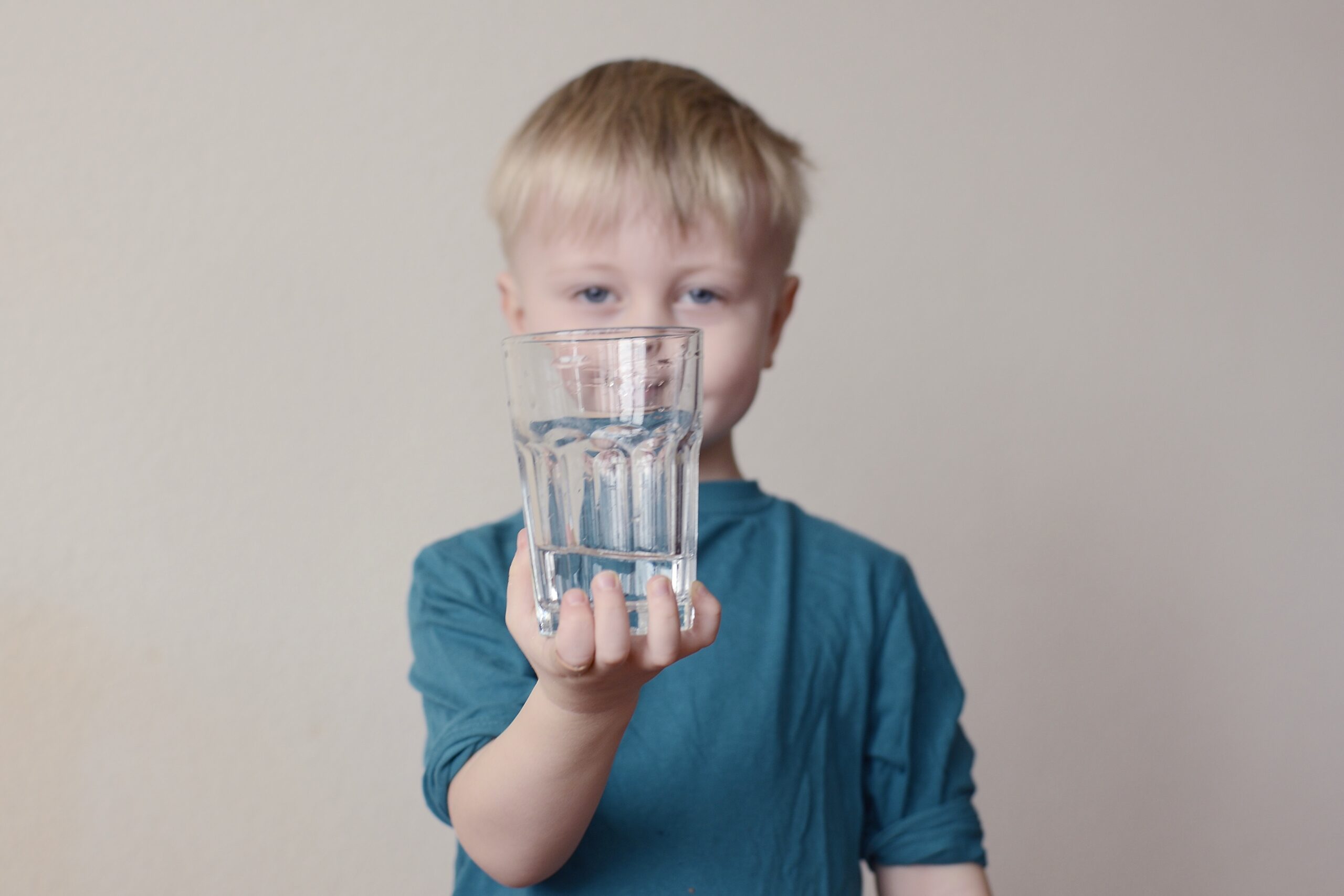 Sarışın erkek çocuk eliyle su bardağını alttan tutup havaya kaldırıyor