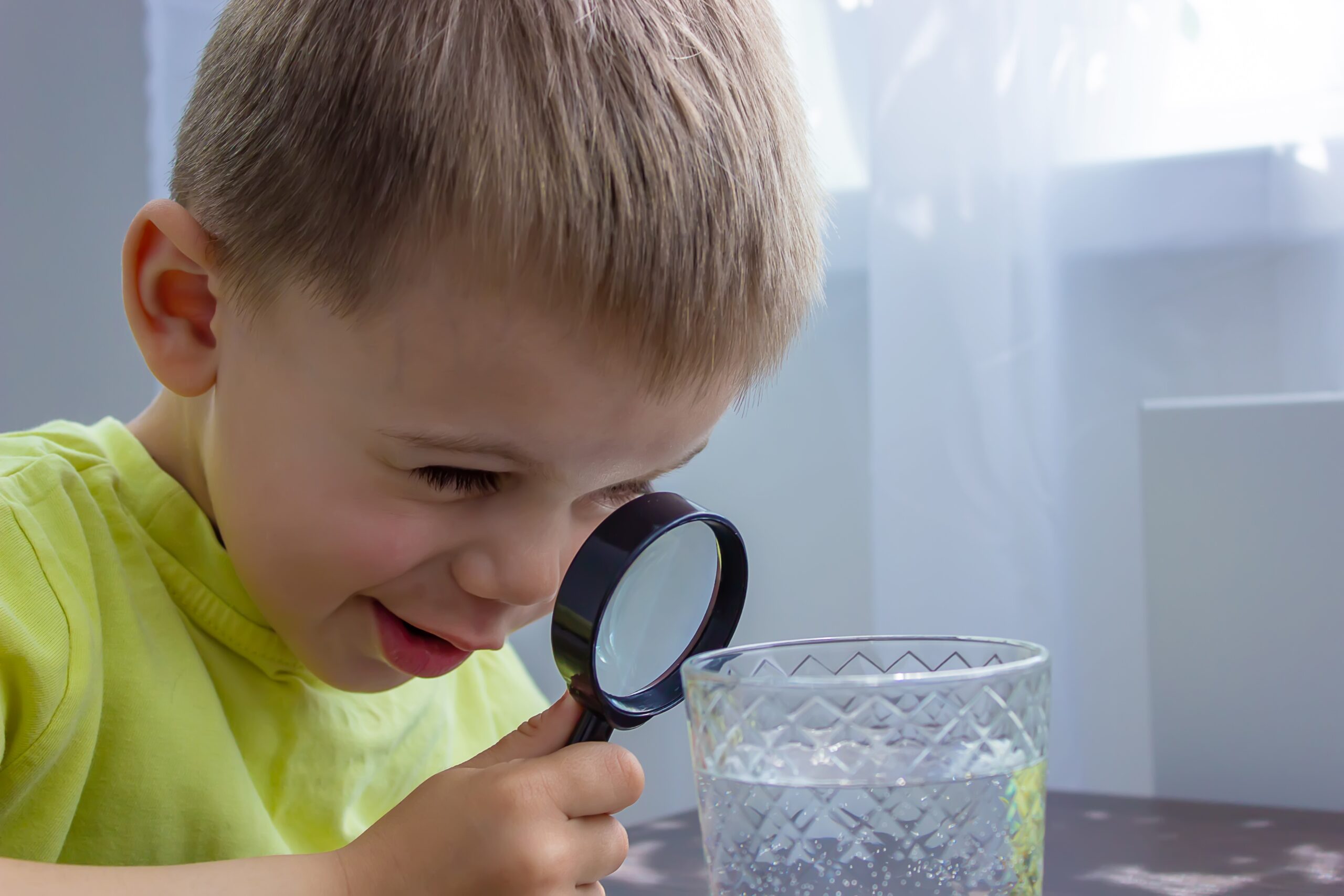 Erkek çocuk bir bardak suyu büyüteç ile inceliyor